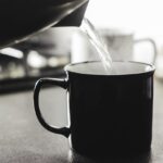 Una tazza di acqua calda fumante su un tavolo, simbolo di benessere e idratazione al mattino.