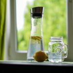 Un bicchiere d'acqua con gocce di condensa su sfondo blu, simbolo dell'importanza di idratarsi.