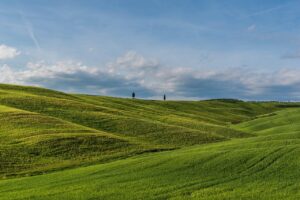 Panorama della Val d'Orcia con colline verdi, cipressi e un cielo azzurro, simbolo della bellezza toscana.