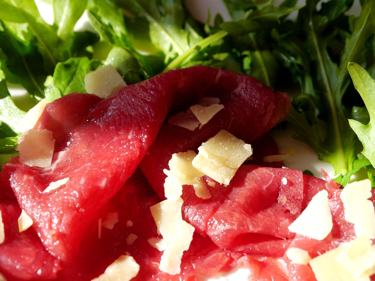 Bresaola appoggiata su un tagliere, con fette sottili e guarnita con rucola e scaglie di formaggio.