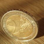 Monete da 2 euro ritirate, esposte su un tavolo con un cartello che indica il loro valore attuale.